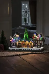 Decoración Navideña Mecánica Con Mercado Navideño 24cm Multicolor De Konstsmide - Con 28 luces LED de color blanco c&aacute;lido, casas cubiertas de nieve, puestos de mercado coloridos y un majestuoso &aacute;rbol de Navidad en el centro, difunde luz y m&uacute;sica.