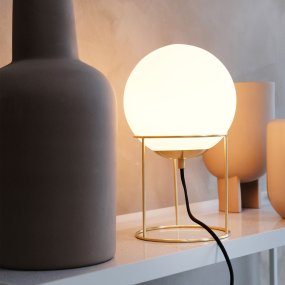 Madrid 34cm Latón lámpara de mesa De Dyberg Larsen - Madrid es una lámpara de mesa moderna que combina elegancia y sencillez con su pantalla redonda de cristal blanco opalino y su elegante marco de latón.
