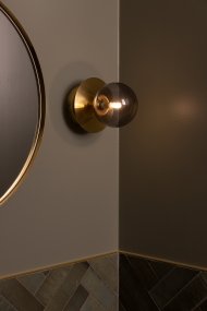 Art Deco Ø16 Latón cepillado/ahumado lámpara de baño De Globen Lighting - Está hecha de metal y su pantalla de cristal ahumado crea una hermosa iluminación en la habitación.