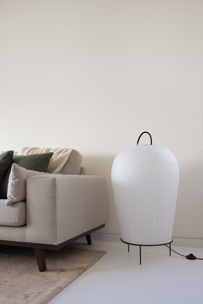 Osaka Blanco lámpara de pie De Globen Lighting - La lámpara está hecha de papel de arroz blanco y tiene un mango decorativo de metal pintado en negro mate y un soporte a juego en la parte inferior sobre el que descansa la pantalla de papel.