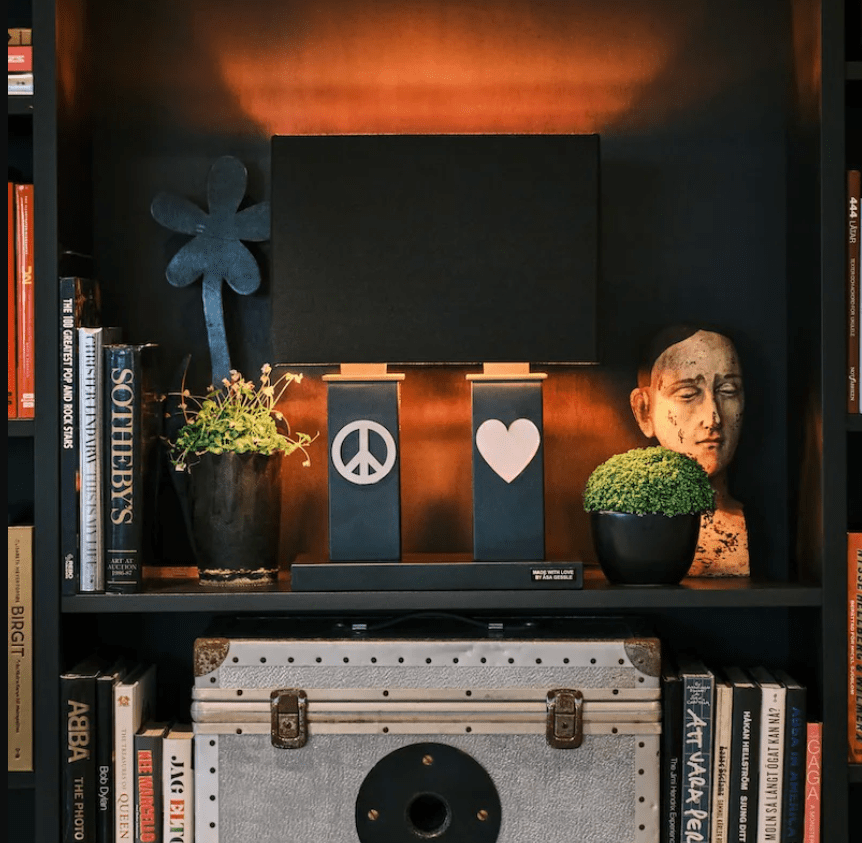 Stand By Me 50cm Negro lámpara de mesa De By Rydéns - La amplia pantalla de tela negra contrasta con las columnas m&aacute;s estrechas de la base de la l&aacute;mpara, ambas decoradas con un s&iacute;mbolo de metal, un signo de la paz en un lado y un coraz&oacute;n en el otro.