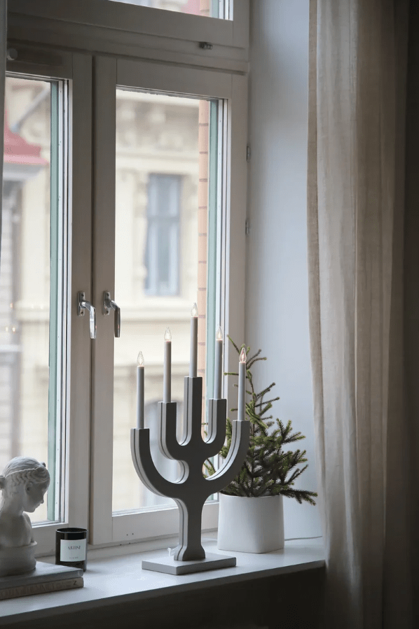 Sapin 5L Greige De Markslöjd - Su generoso tama&ntilde;o lo convierte en un elemento decorativo que atrae todas las miradas, especialmente en ventanas grandes, donde las cinco velas proyectan una luz c&aacute;lida y acogedora en las oscuras noches de invierno.