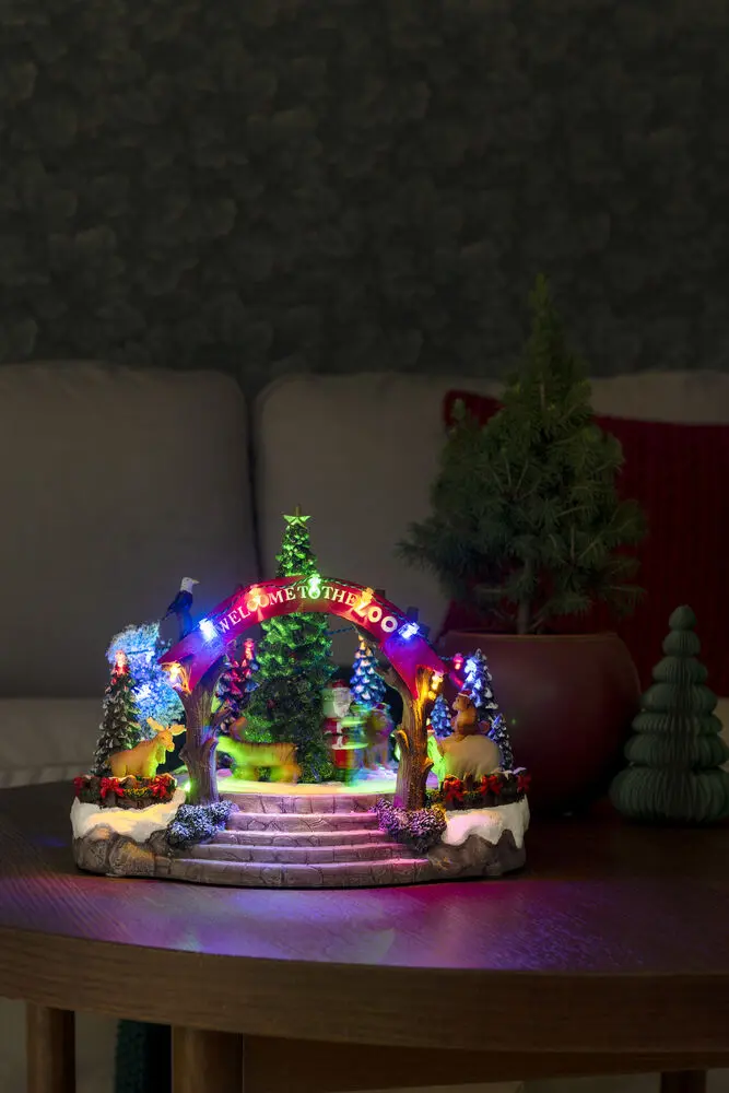 Decoración Navideña Mecánica Con Zoológico 20cm Multicolor De Konstsmide - Esta decoraci&oacute;n navide&ntilde;a mec&aacute;nica presenta una escena colorida con 19 luces LED de color blanco c&aacute;lido, m&uacute;sica, animales y Pap&aacute; Noel alrededor de un &aacute;rbol de Navidad brillante.