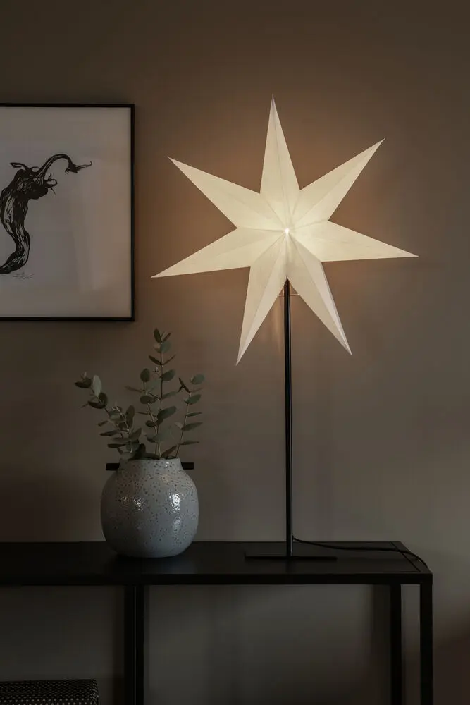 Estrella De Papel Ø50 Blanco De Konstsmide - La elegante estrella blanca reposa sobre un elegante soporte de metal negro y emite una luz suave y agradable.