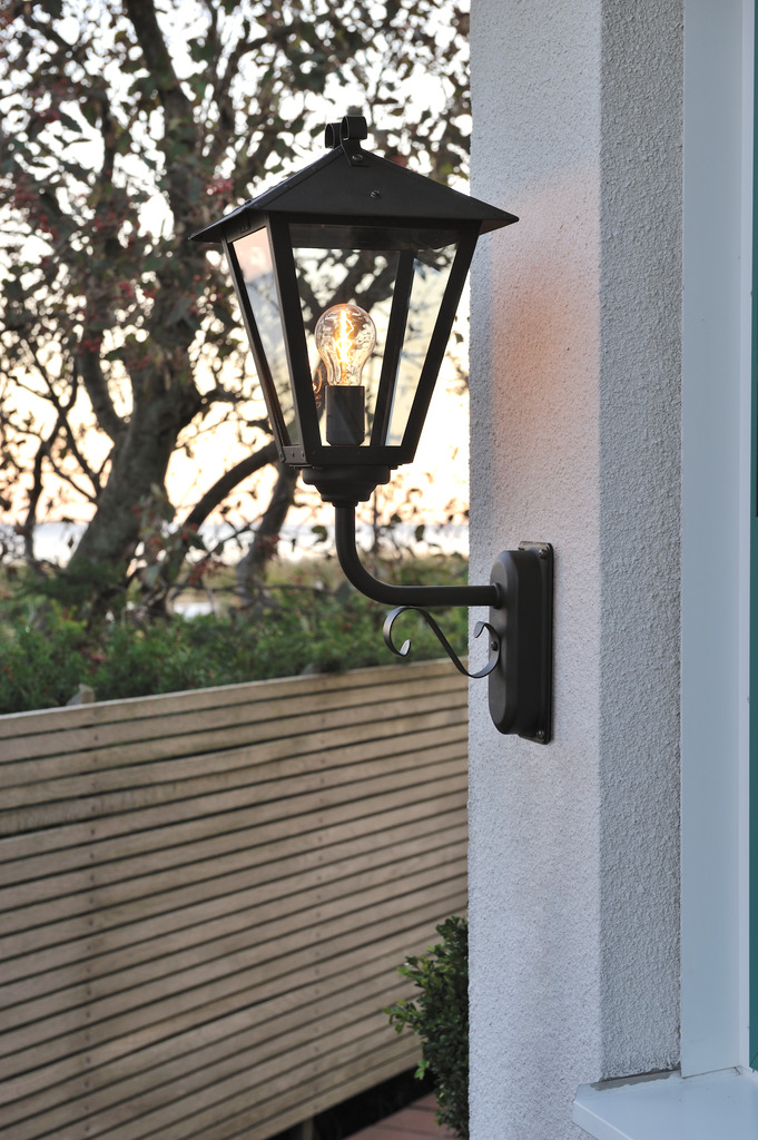 Benu Negro lámpara de exterior De Konstsmide - La forma cl&aacute;sica de linterna y los materiales robustos hacen de esta l&aacute;mpara la elecci&oacute;n perfecta para cualquiera que quiera crear un ambiente acogedor en zonas de entrada o pasillos largos.
