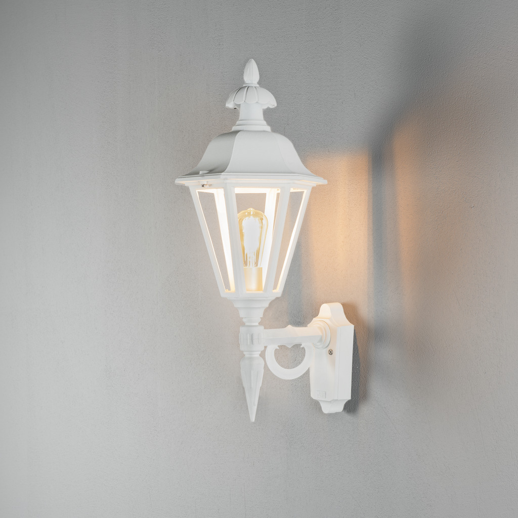 Pallas Blanco lámpara de exterior De Konstsmide - Con su diseño en forma de linterna y paneles de vidrio transparente, la lámpara emite una luz cálida y acogedora que es perfecta para entradas, patios y pasillos.