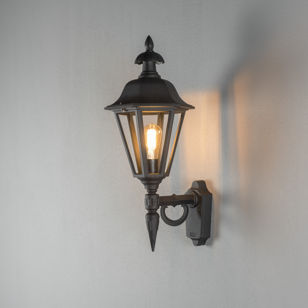 Pallas Negro lámpara de exterior De Konstsmide - Con su diseño en forma de linterna y paneles de vidrio transparente, la lámpara emite una luz cálida y acogedora que es perfecta para entradas, patios y pasillos.