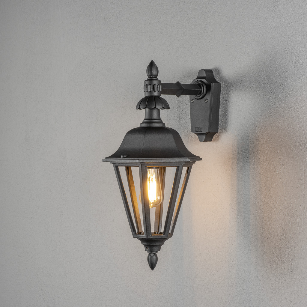 Pallas Negro lámpara de exterior De Konstsmide - Con su diseño en forma de linterna y paneles de vidrio transparente, la lámpara emite una luz cálida y acogedora que es perfecta para entradas, patios y pasillos.