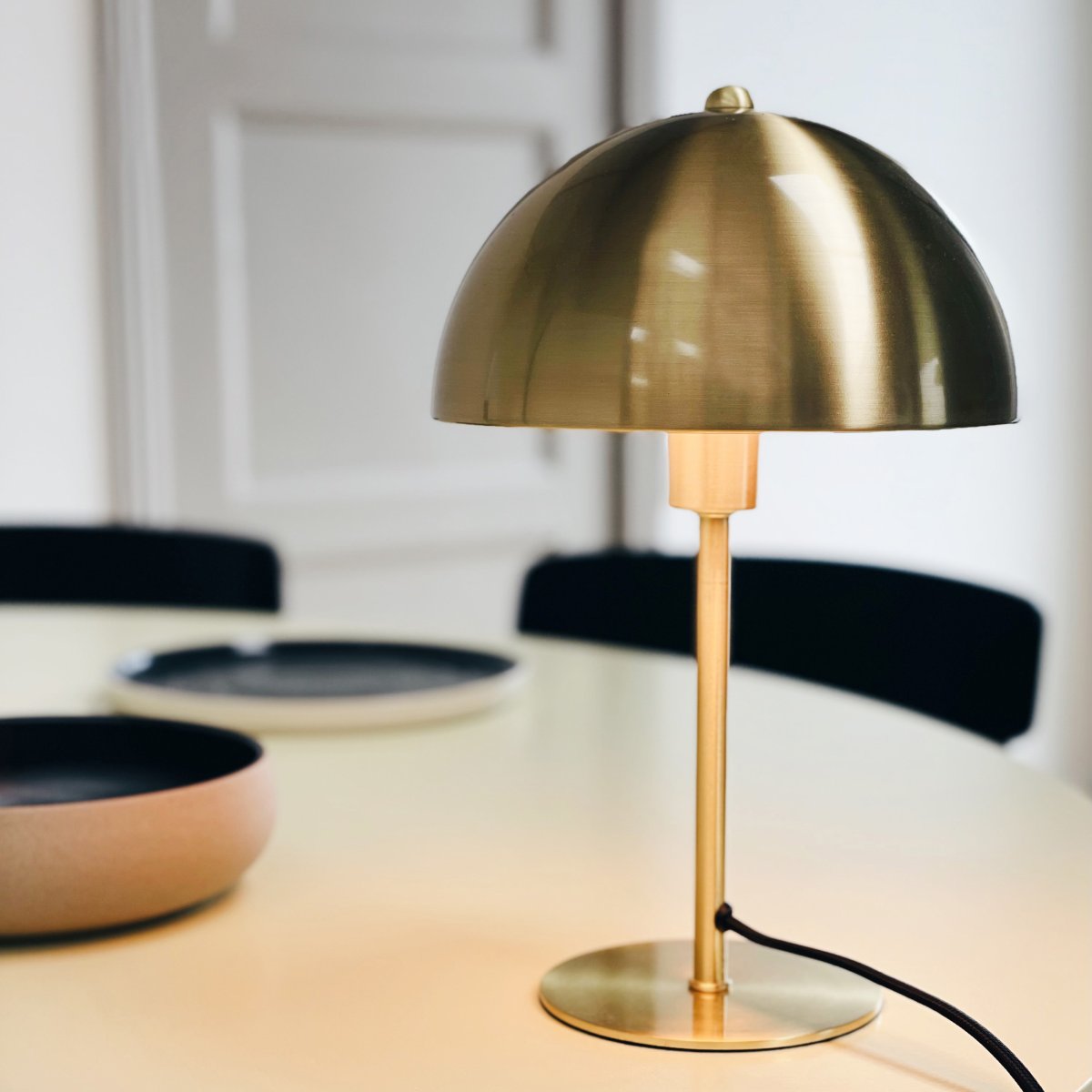 Lyon 30cm Latón lámpara de mesa De Dyberg Larsen - La pantalla semicircular añade un toque moderno y garantiza una distribución de la luz agradable y uniforme, ideal tanto para la iluminación de tareas como para la iluminación ambiental.