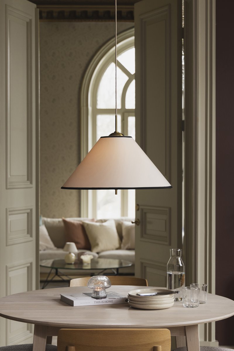 Iris Ø50 Blanco cremoso Lámpas de techo De Globen Lighting - La elegante lámpara colgante Iris, fabricada en hierro con acabado de latón y con una pantalla de algodón color crema hecha a mano, cautiva por su diseño clásico y sus detalles decorativos de latón, convirtiéndola en un impresionante elemento central, por ejemplo, sobre una mesa de comedor.