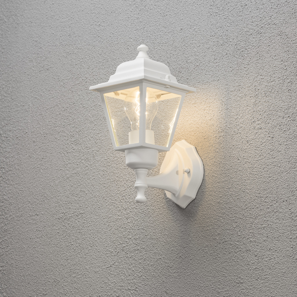 Vägglykta Blanco lámpara de exterior De Konstsmide - Con su diseño en forma de linterna y paneles de vidrio transparente, la lámpara emite una luz cálida y acogedora que es perfecta para entradas, patios y pasillos.