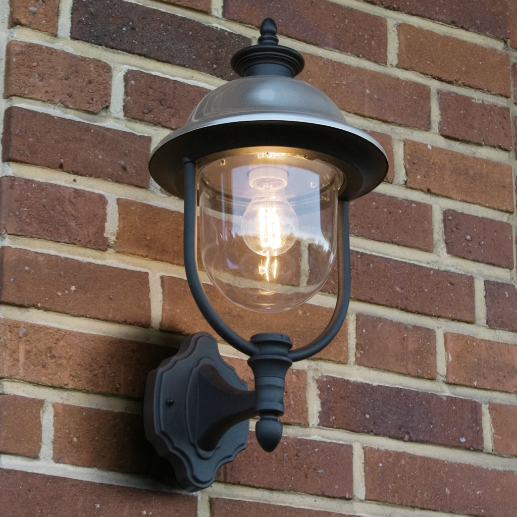 Parma Negro lámpara de exterior De Konstsmide - Con su robusta superficie negra y su pantalla de cristal transparente, emite una luz cálida y acogedora, creando un ambiente acogedor en la entrada o en la terraza.