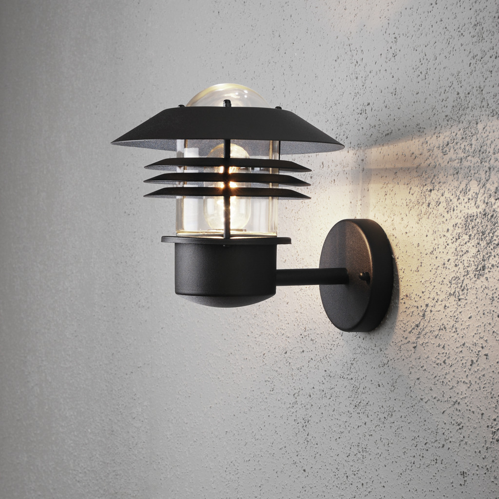 Modena Negro lámpara de exterior De Konstsmide - Con su techo protector y su elegante diseño, proporciona una luz agradable y dirigida, ideal para crear un ambiente seguro y acogedor al aire libre.