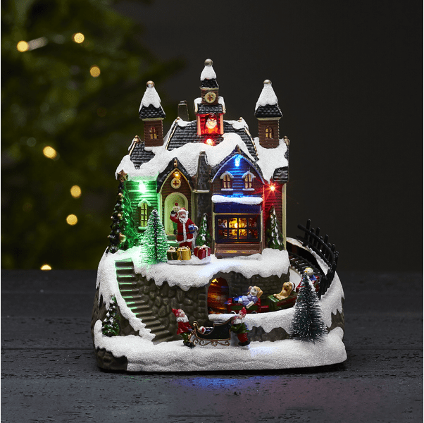 Trainville Multicolor De Star Trading - Pueblo navideño decorativo compuesto por casas con torres, ventanas luminosas y llamativas, y un Papá Noel de pie saludando.