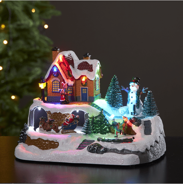 Winterville Multicolor De Star Trading - Una preciosa decoraci&oacute;n navide&ntilde;a con un mu&ntilde;eco de nieve observando a los ni&ntilde;os patinar y Pap&aacute; Noel con su trineo y renos.