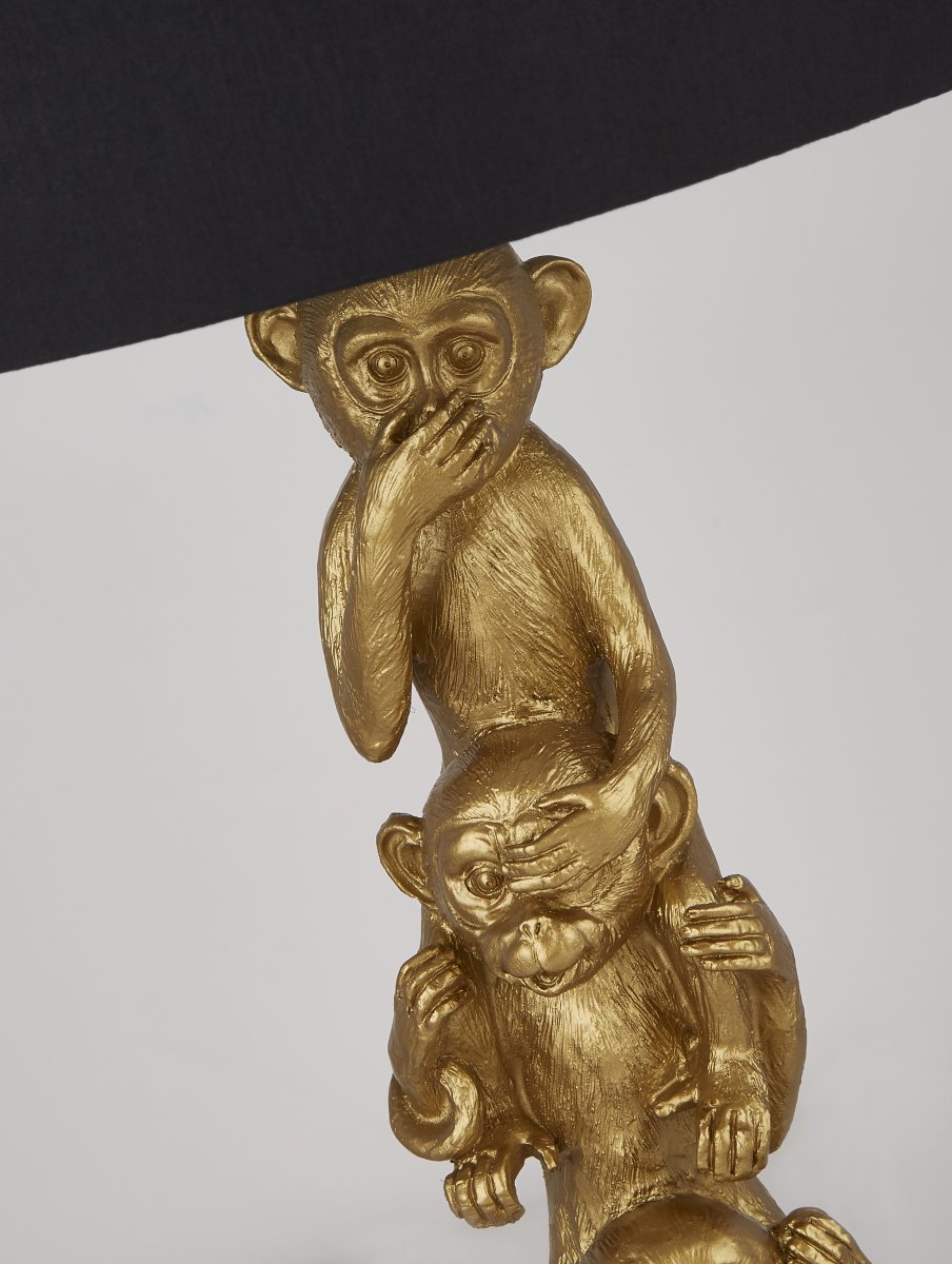 Monkey 40cm Oro lámpara de mesa De Searchlight - Esta encantadora lámpara de mesa presenta un mono detallado sobre un marco dorado con una pantalla negra y un interior blanco.