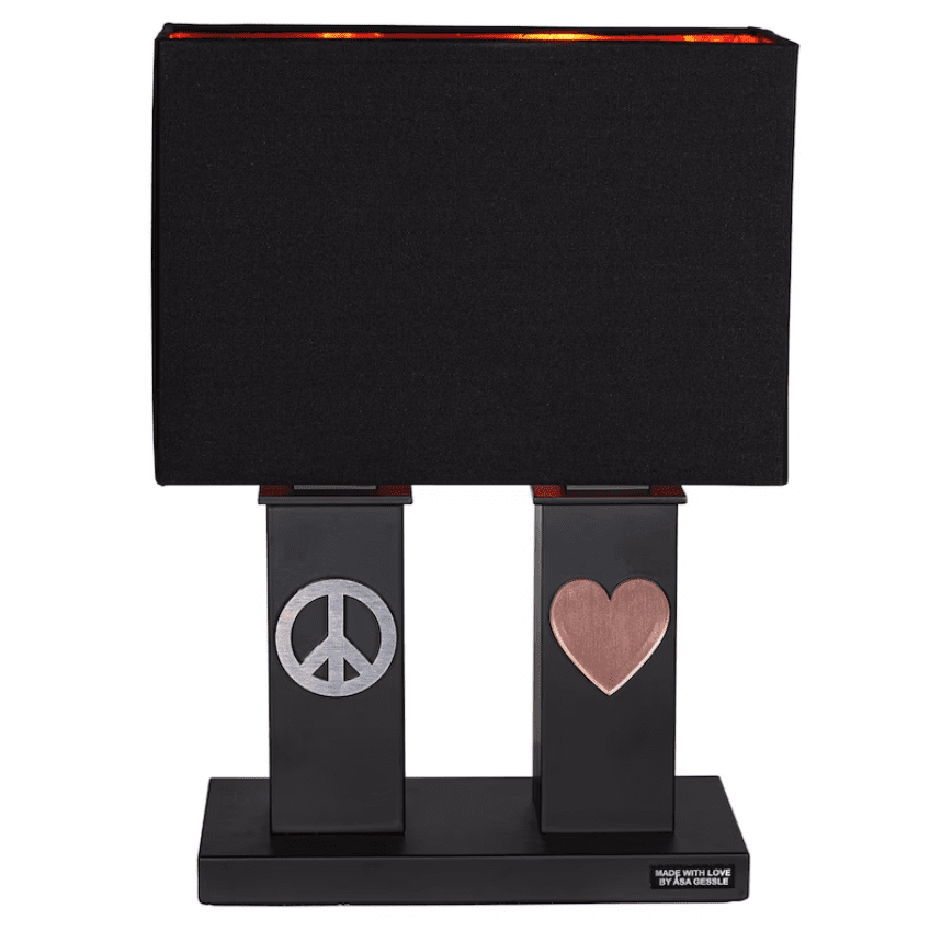 Stand By Me 50cm Negro lámpara de mesa De By Rydéns - La amplia pantalla de tela negra contrasta con las columnas m&aacute;s estrechas de la base de la l&aacute;mpara, ambas decoradas con un s&iacute;mbolo de metal, un signo de la paz en un lado y un coraz&oacute;n en el otro.