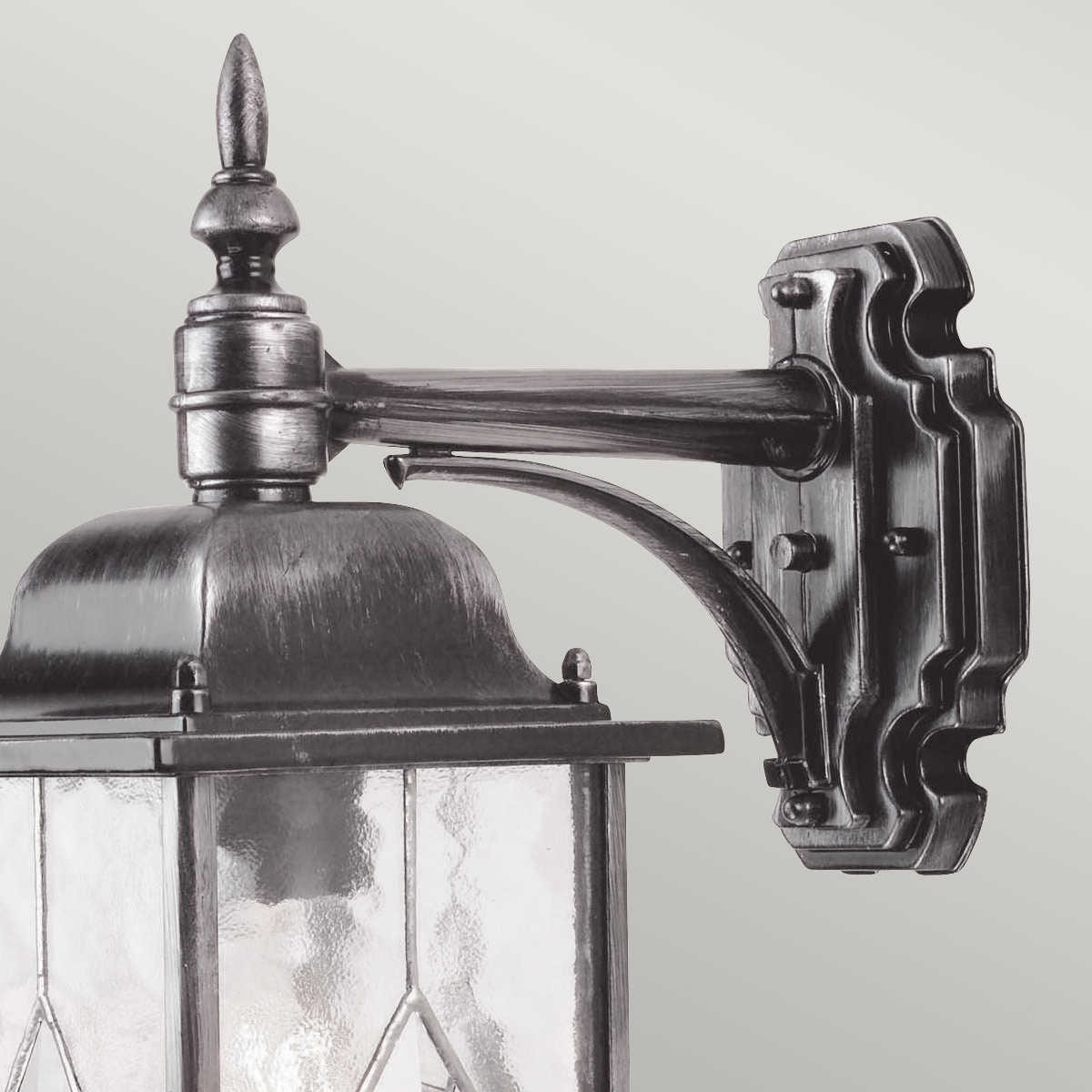 Wexford Plata lámpara de exterior De Elstead Lighting - Wexford es una lámpara de pared clásica para exteriores, fabricada en aluminio con un elegante acabado en plata oscura y elementos decorativos de vidrio con textura de vidrieras emplomadas.